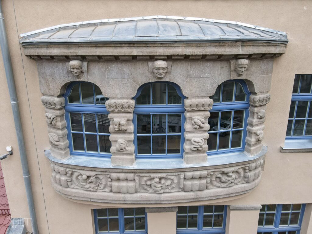 Na zdjęciu fragment zabytkowej elewacji z oknem z ramami w kolorze niebieskim oraz z płaskorzeźbami