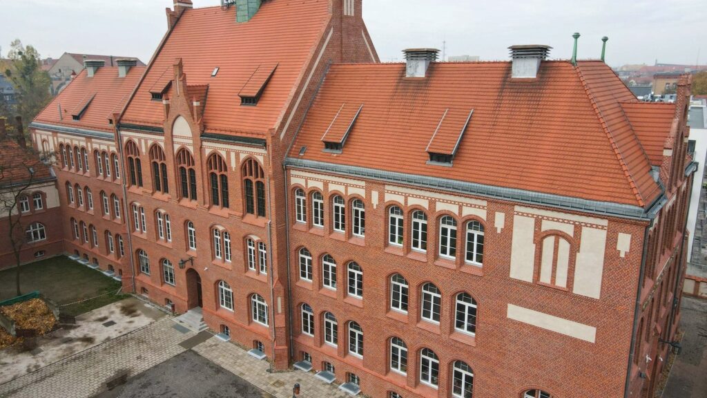 Na zdjęciu budynek Zespołu Szkół Ogólnokształcących nr 1. Elewacja z czerwonej cegły. Półokrągłe białe okna. Dach z czerwonej dachówki.