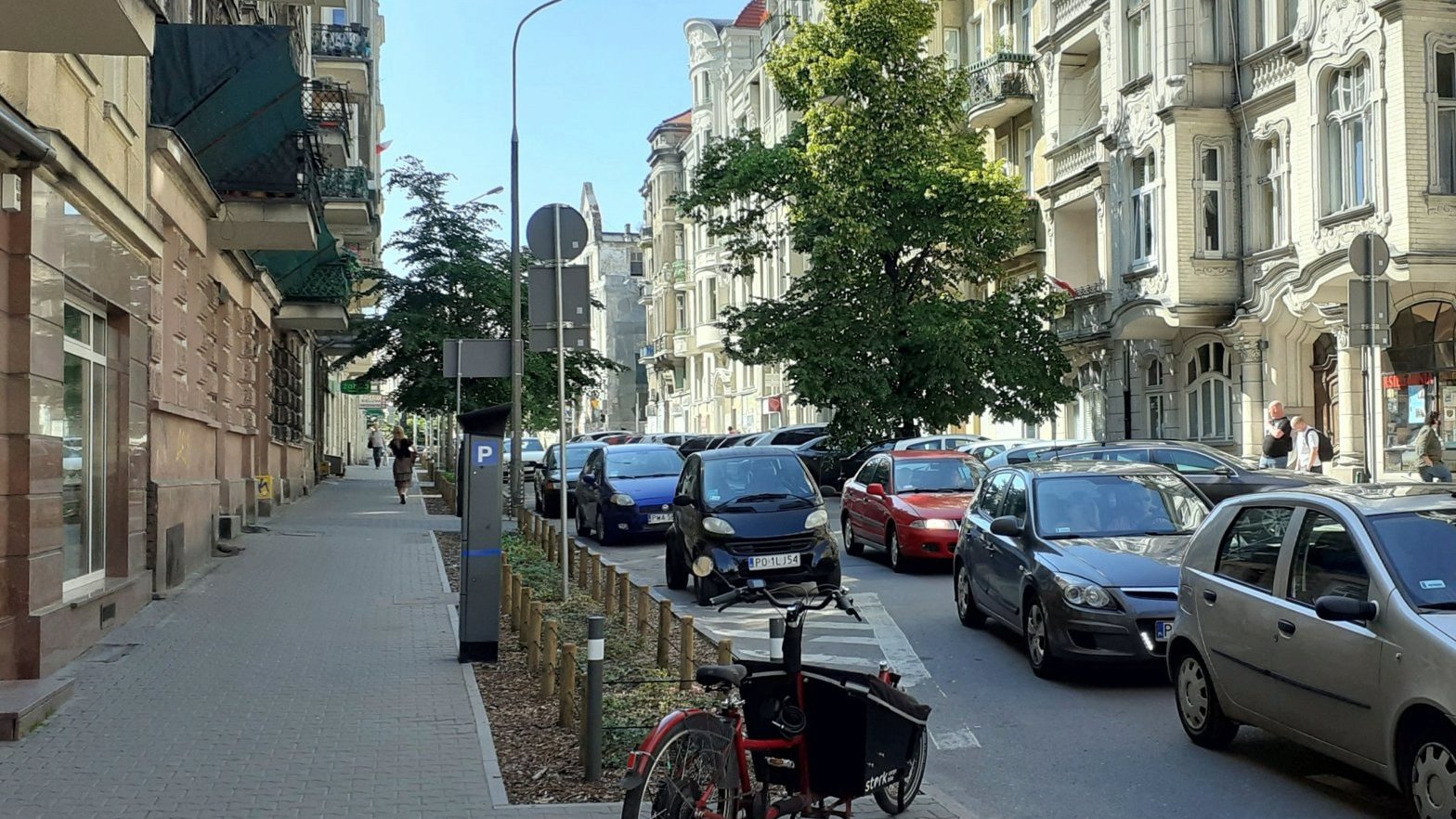 ulica z zabytkowymi budynkami, auta na jedni i nowo posadzona zieleń