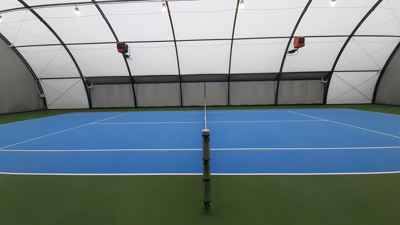 Na zdjęciu zadaszony kort do tenisa ziemnego. Nawierzchnia w kolorze niebieskim
