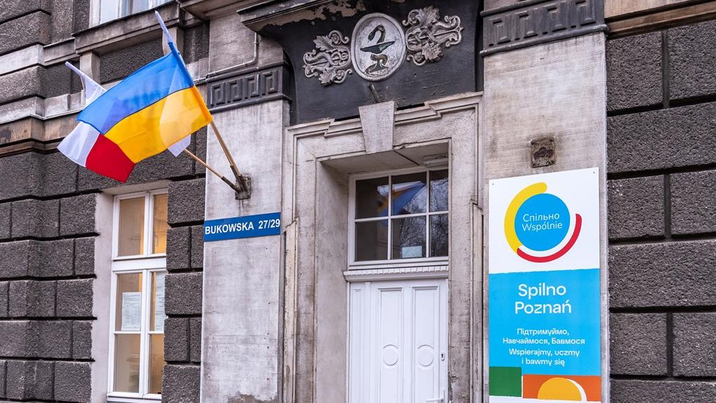 Widok na wejście do budynku, w którym mieści się Spilno Poznań, z tablicą i flagami: polską i ukraińską