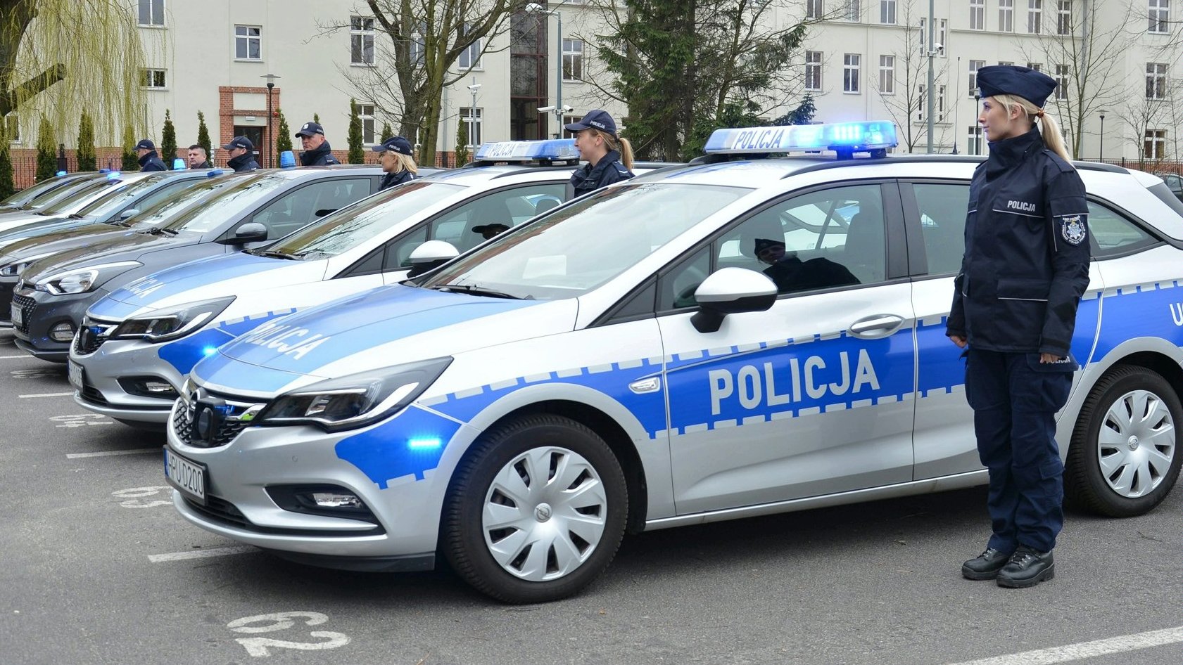 Policjantki i policjanci stojący przy samochodach służbowych