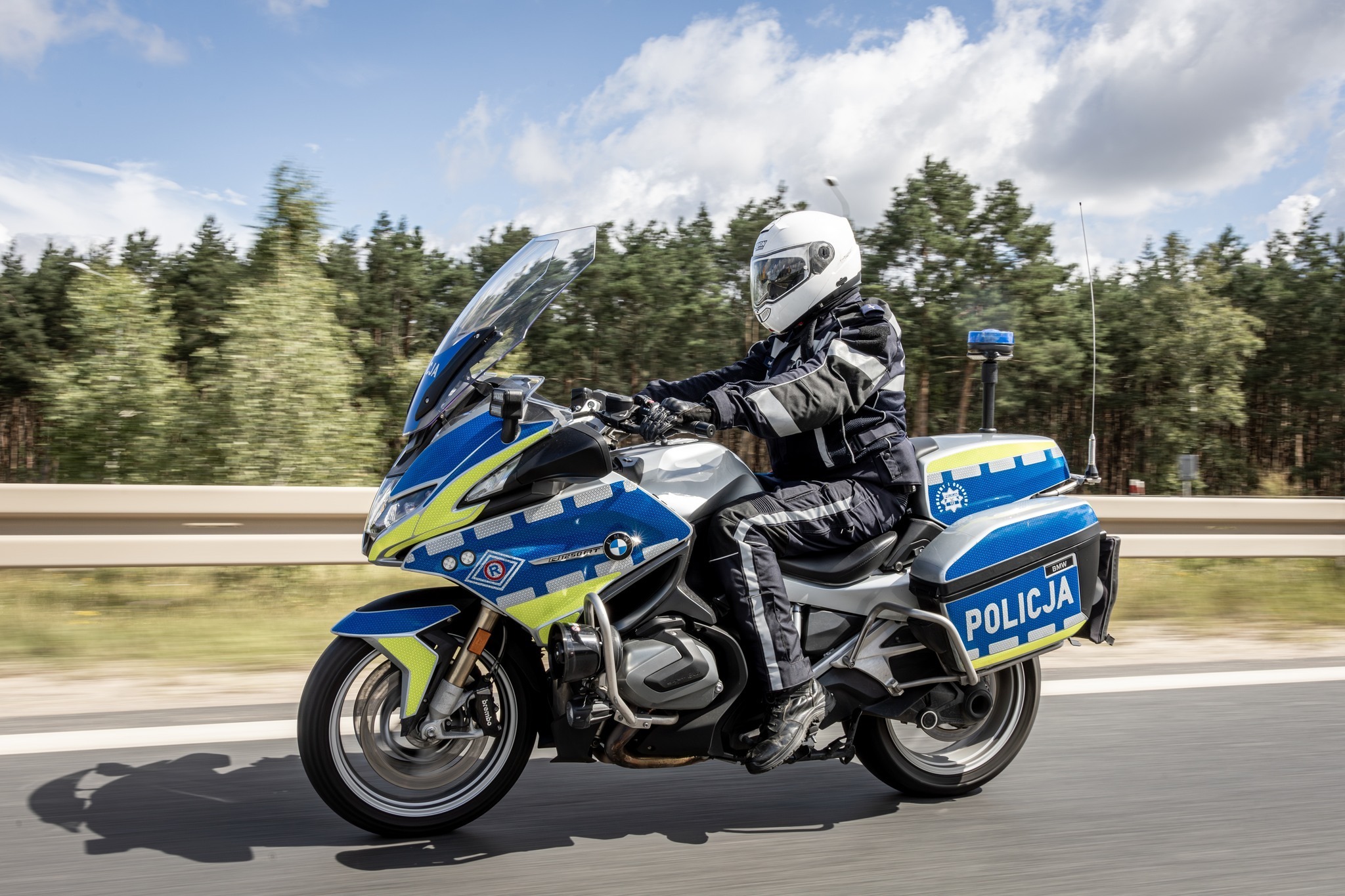Policjant jedzie na motocyklu, z tyłu las