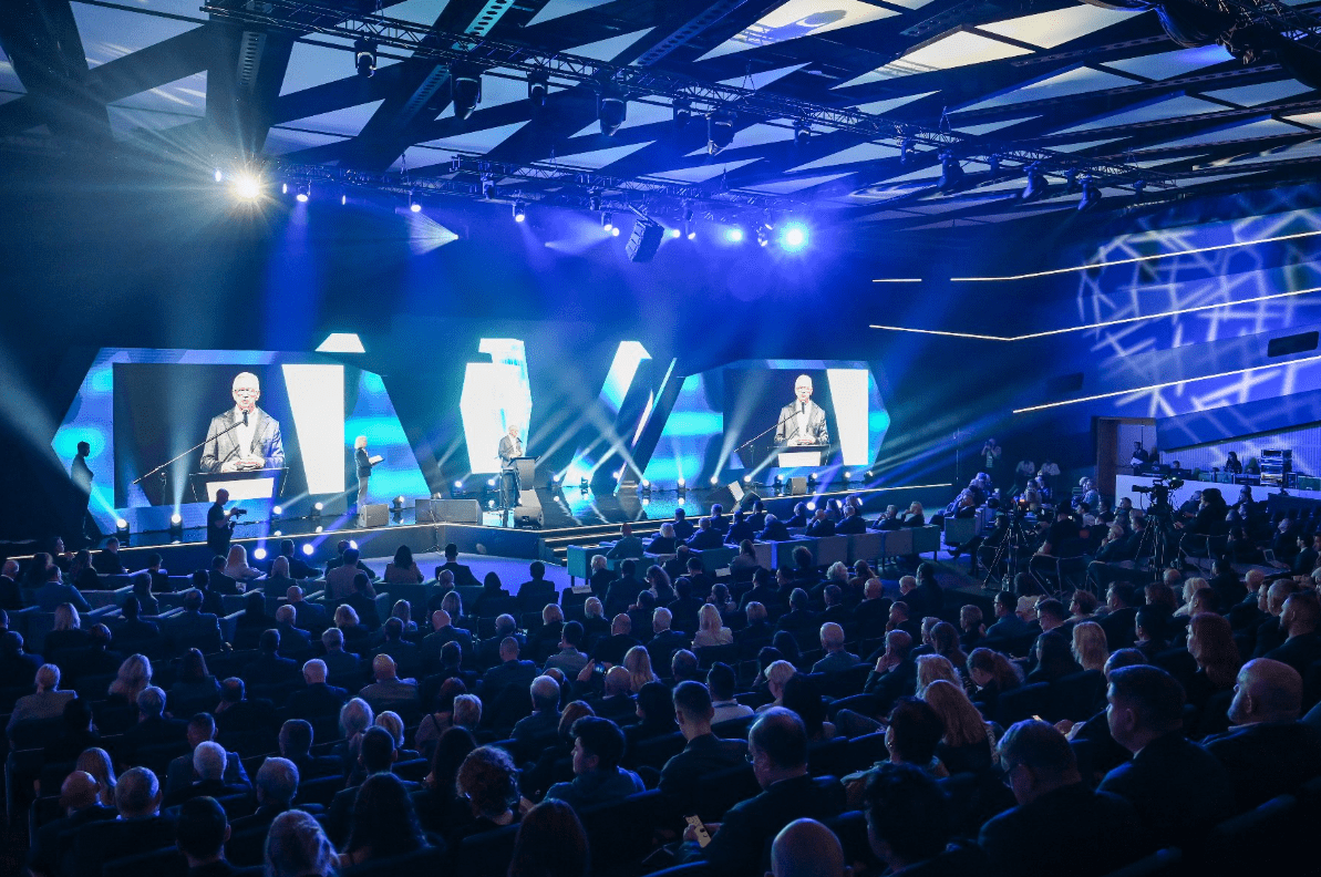 Pełna widownia uczestników na Local Trends 2024, prezydent Poznania Jacek Jaśkowiak przemawia na scenie. Niebieskie światło i ekrany w tle.
