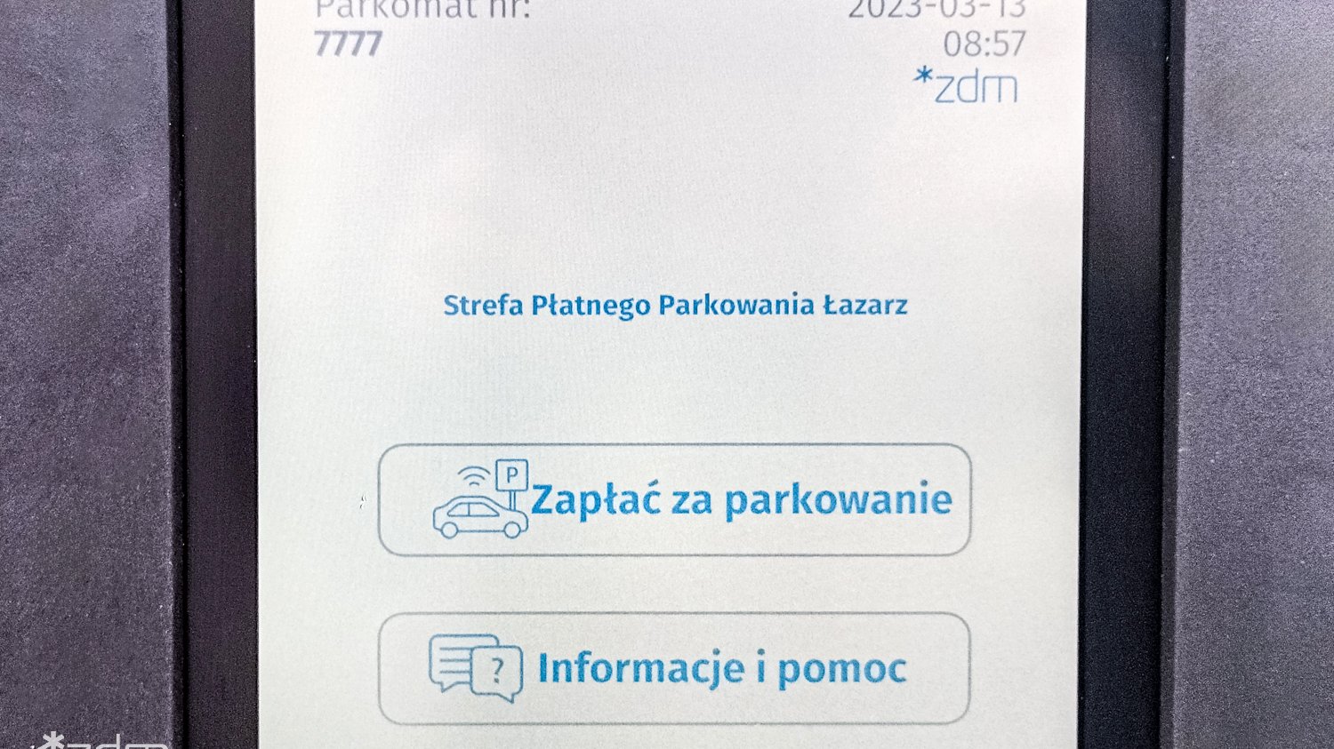 Ekran parkomatu pokazujący możliwe opcje do wyboru. Opcja "Zapłać za parkowanie" oraz opcja "Informacje i pomoc". Numer parkomatu po lewej stronie, data i godzina po prawej stronie.