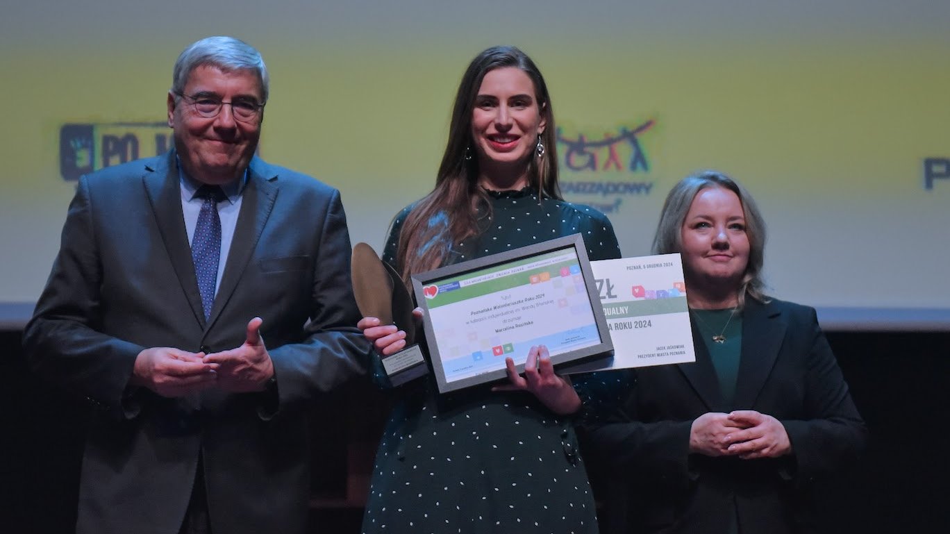 Trójka osób w formalnych ubraniach, w środku Marcelina Rosińska z nagrodami za wyróżnienie Poznańskiego Wolontariusza Roku.
