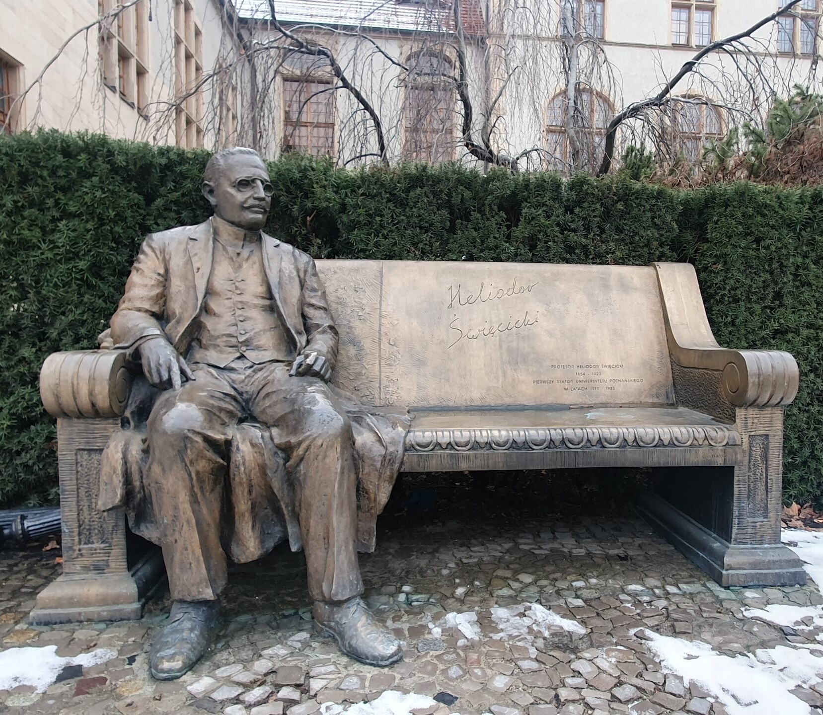 Ławeczka prof. Heliodora Swięcickiego pod Collegium Minus Uniwersytetu im. Adama Mickiewicza w Poznaniu. Odlew postaci profesora siedzi na brzegu ławeczki, obok niego miejsce by usiąść.