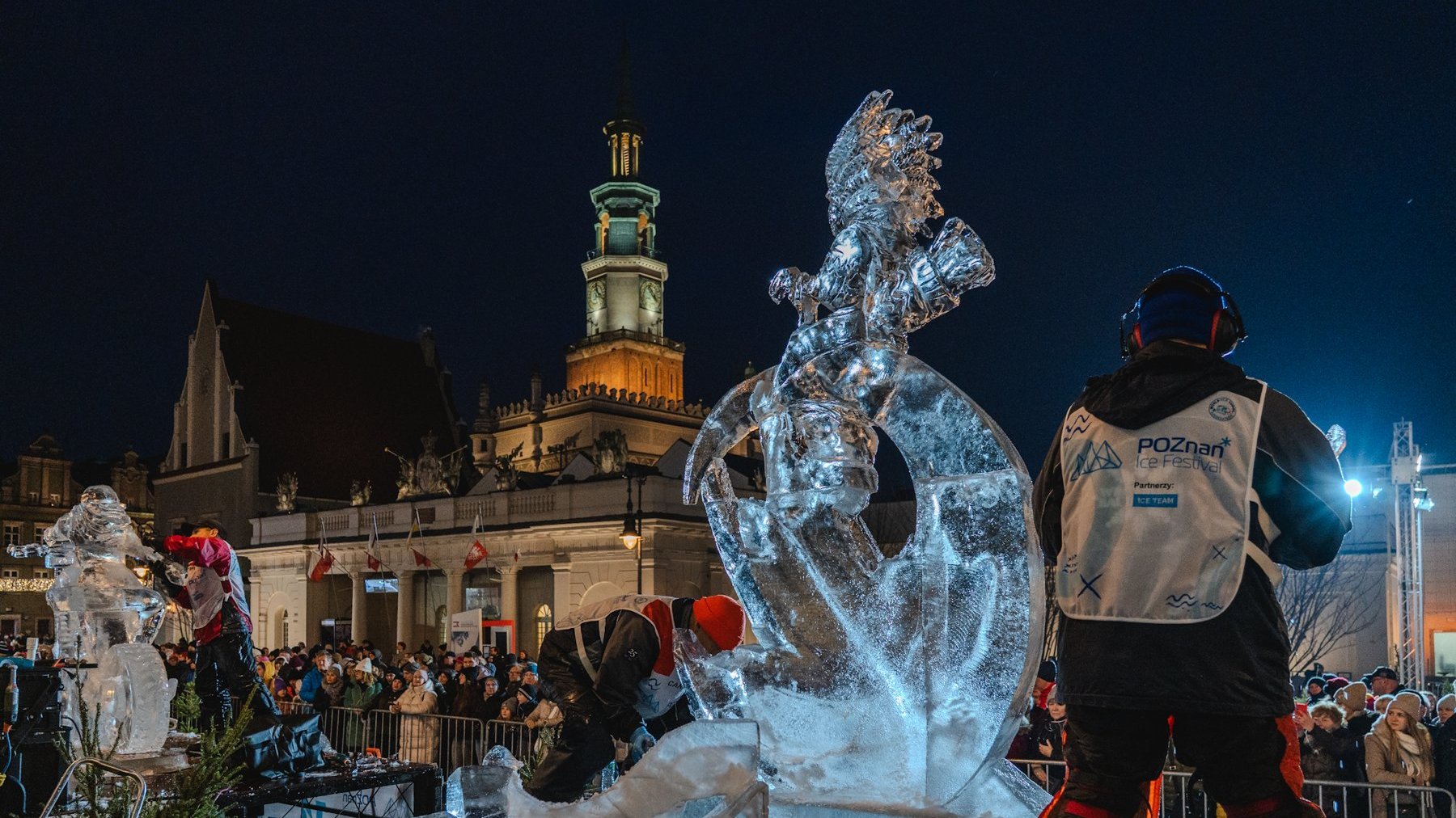 Tworzenie rzeźb lodowych podczas Poznań Ice Festival 2025. Artyści za pomocą narzędzi tworzą rzeźby, w tle mieszkańcy Poznania oraz zabudowa Starego Rynku