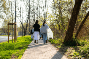 chodnik wśród zieleni, dwie osoby niosą worki na śmieci
